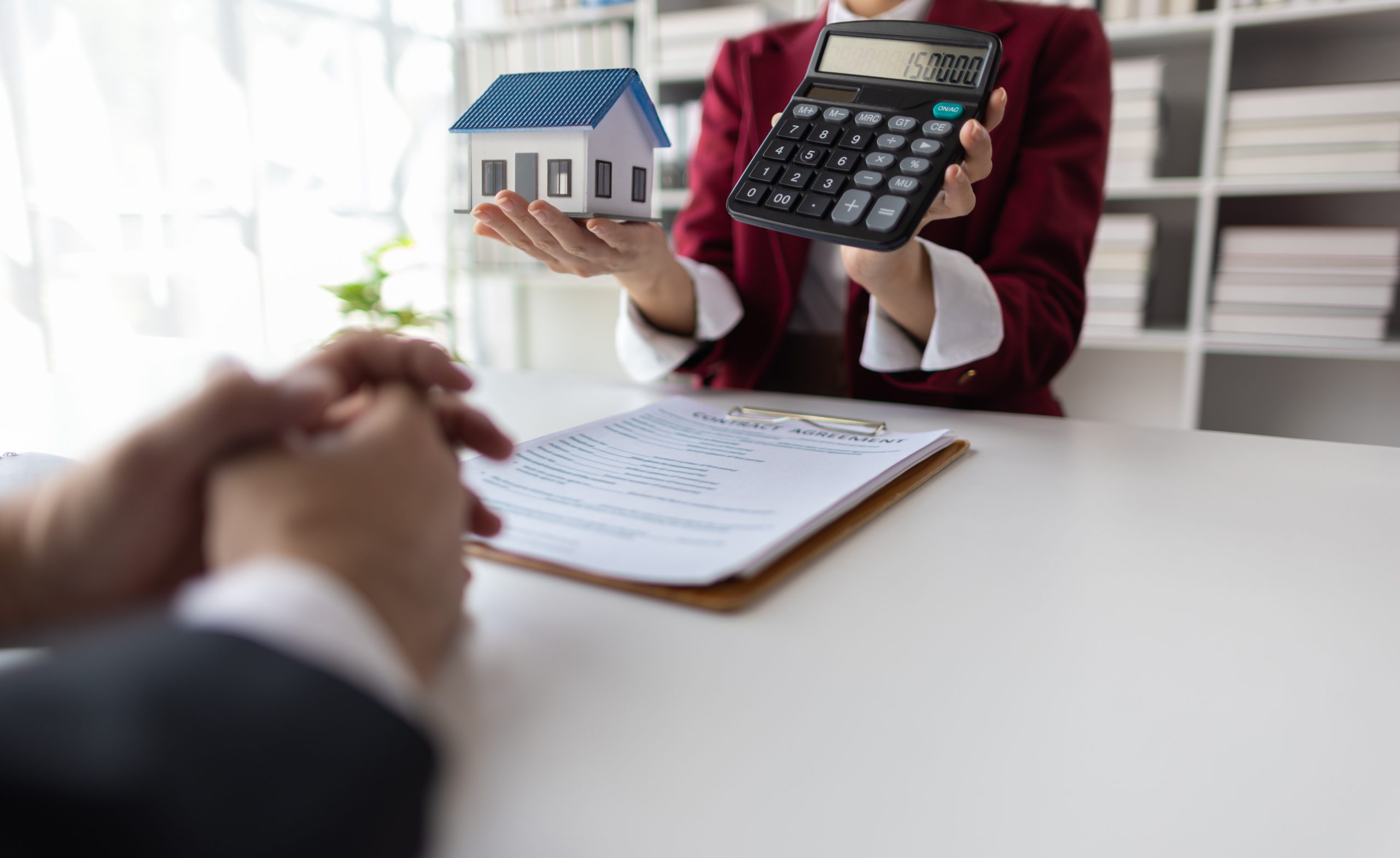 Geschäftsfrau hält ein Modellhaus und einen Taschenrechner in ihren Händen
