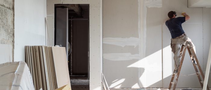 Mann auf einer Leiter saniert die Wände im Inneren eines Hauses